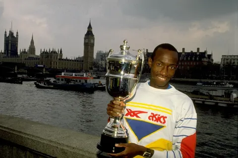 Wakiihuri holding the London Marathon trophy beside the Thames, Big Ben behind, 1989