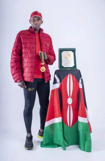 Douglas Wakiihuri holding the 1987 gold medal beside the IAAF plaque and a Kenyan flag