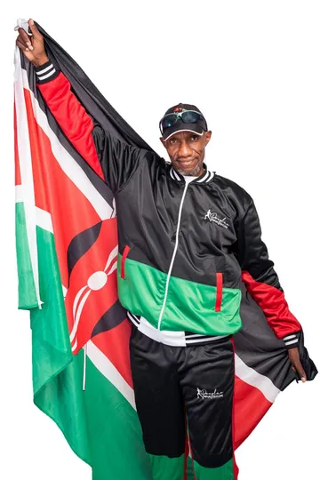 Douglas Wakiihuri in his signature tracksuit holding a Kenyan flag aloft