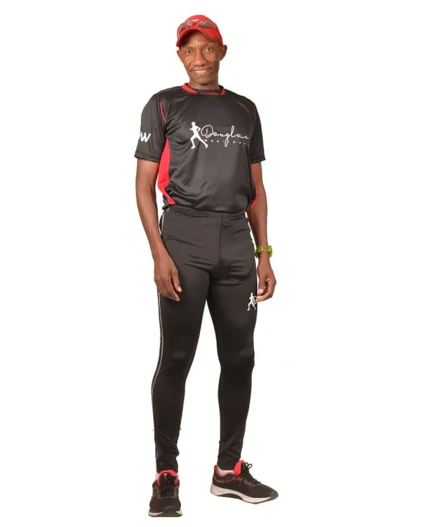 Douglas Wakiihuri standing in his black and red training tee, running tights and red cap, on white